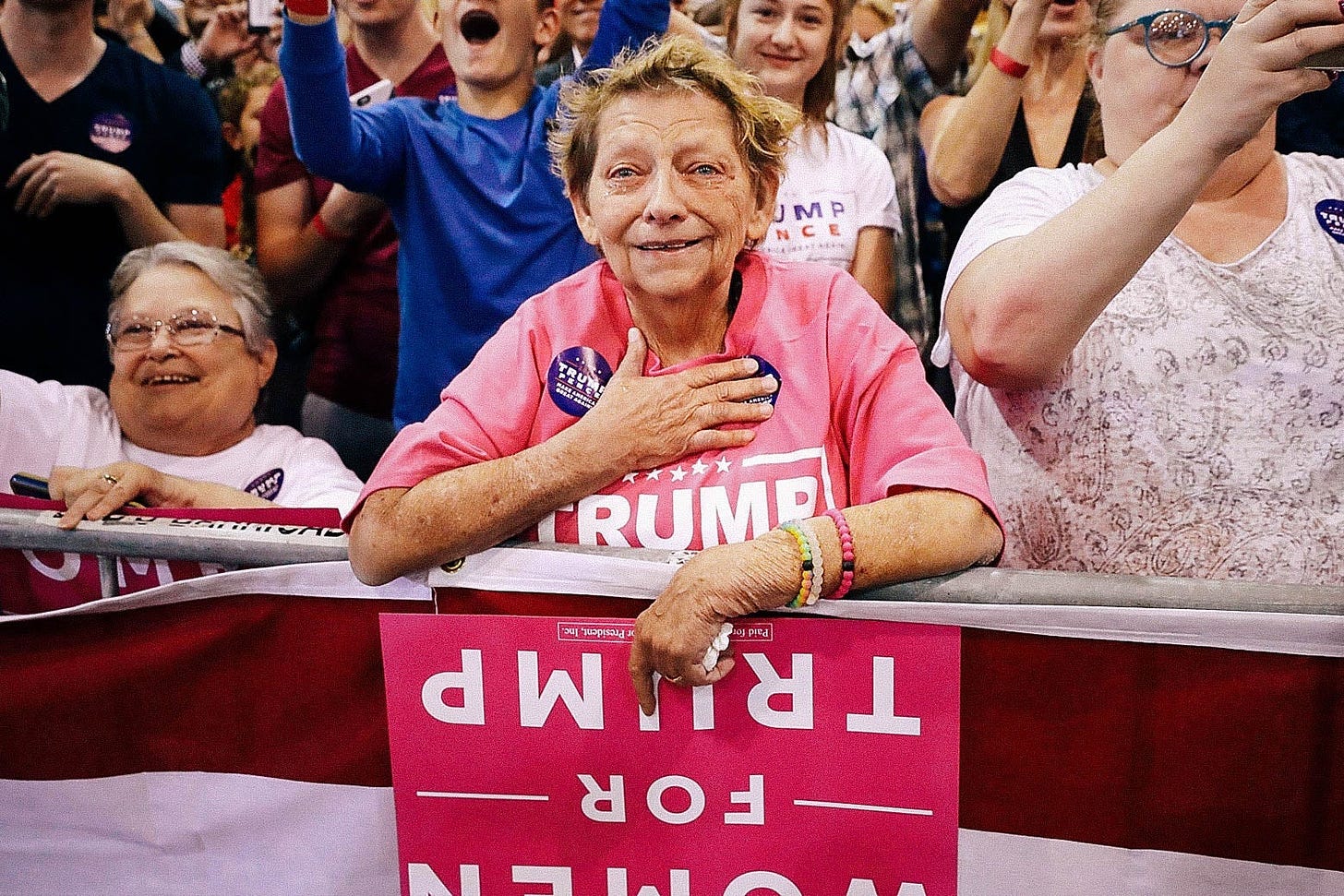 Woman standing in a crowd at a Trump rally holds her hand over her heart, looking emotional