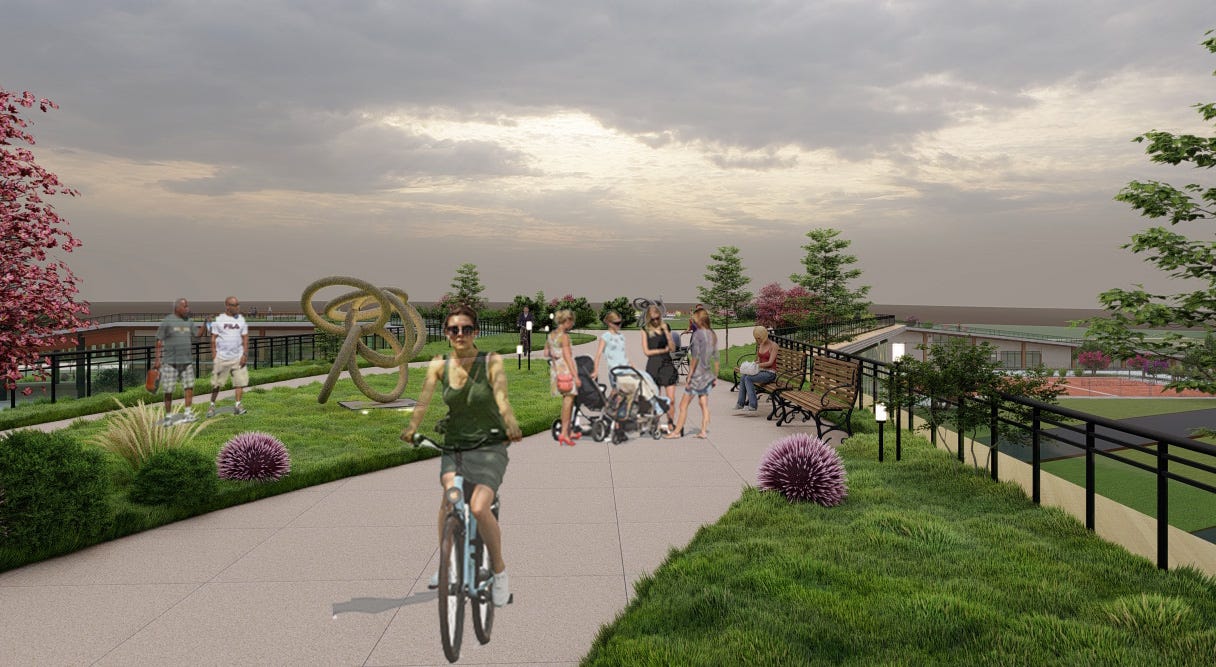 A greenway with bikers, walkers, moms + strollers, benches, with a view beyond to a community center and river