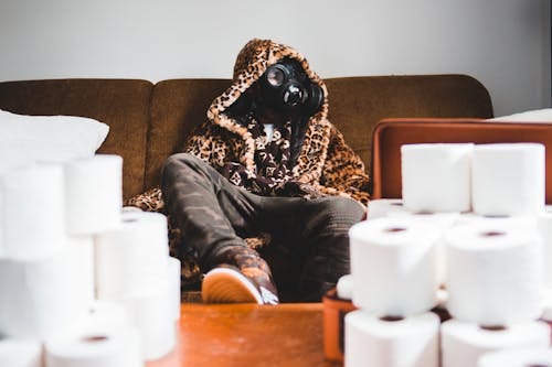 Free A man in a leopard coat with a gas mask surrounded by toilet paper rolls indoors. Stock Photo