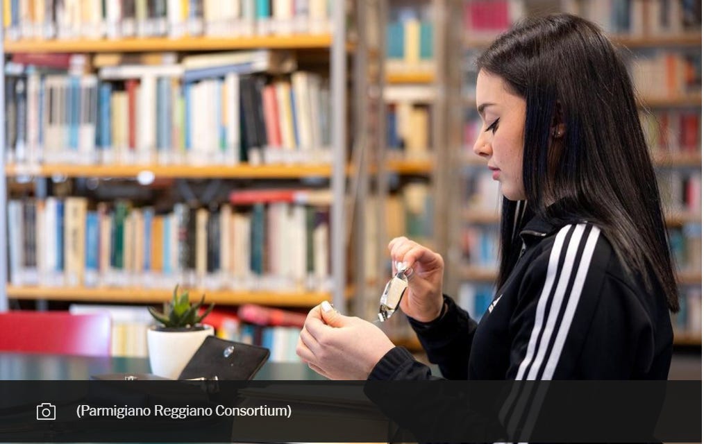 Italian olympic gymnast Giorgia Villa opens an individually wrapped snack of parmigiano reggiano while sitting in a library and wearing an adidas jacket