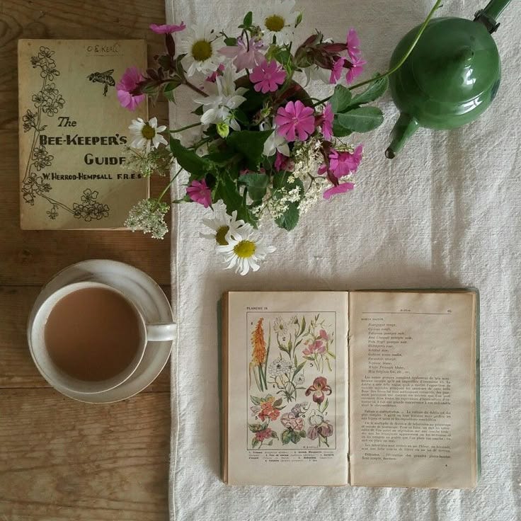 This may contain: a cup of tea next to an open book with flowers in it and a potted plant