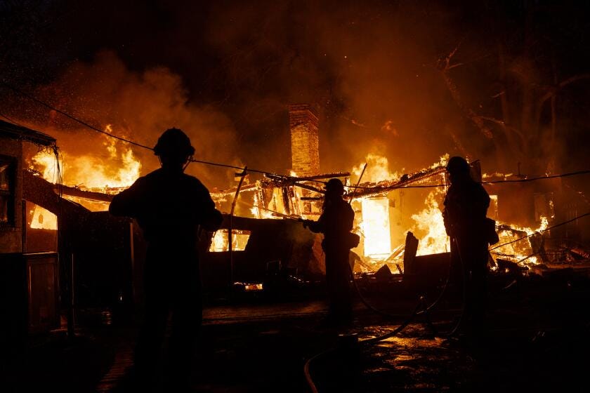 ALTADENA, CA - JANUARY 8, 2025: Firefighters are silhouetted against an engulfed home while keeping the flames from jumping to an adjacent home on Glenrose Avenue during the Eaton fire on January 8, 2025 in Altadena, California. (Gina Ferazzi / Los Angeles Times)