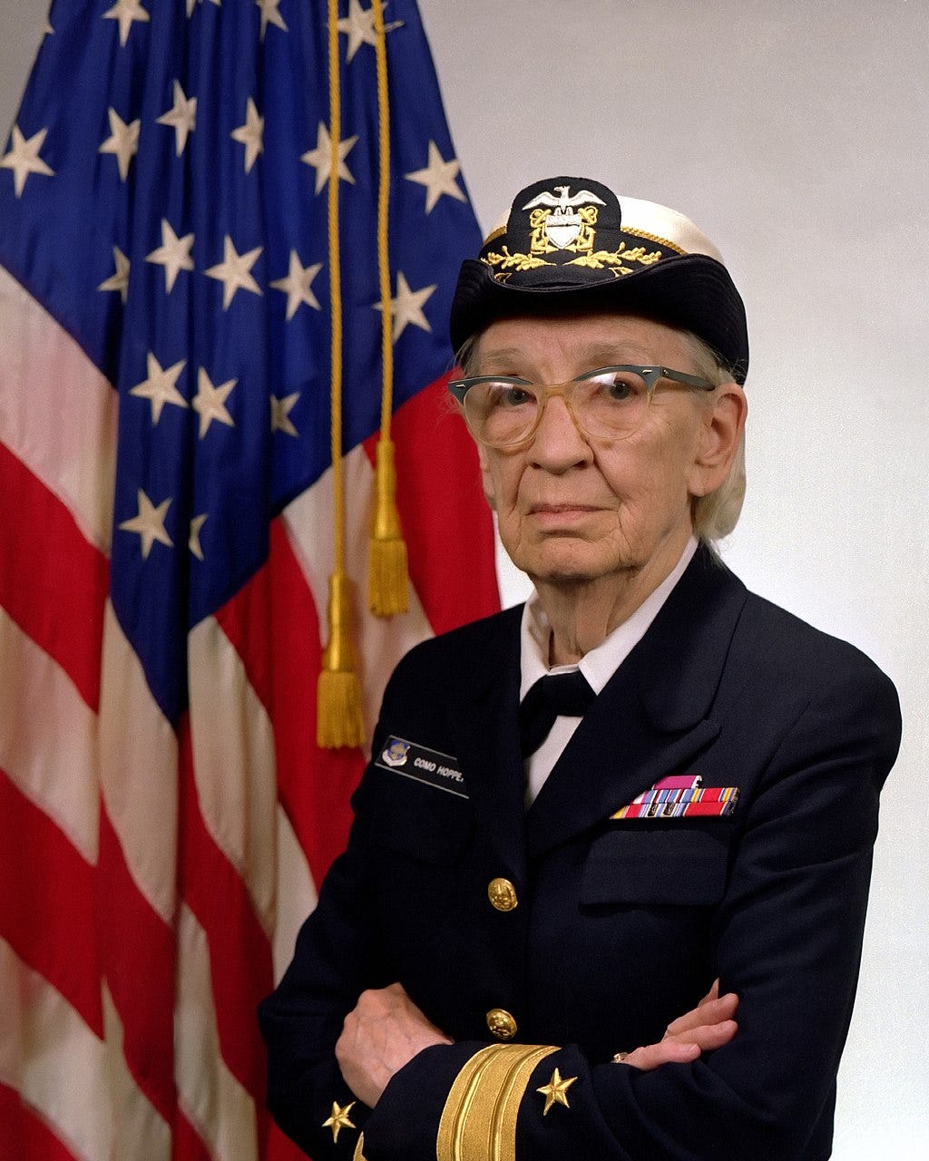 a photo of commodore Grace Hopper in front of an American flag.