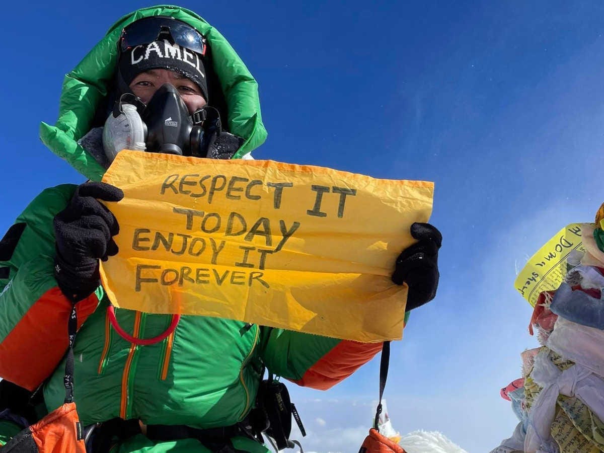 alpinista con una pancarta que dice, en inglés, respétalo hoy, disfrútalo para siempre