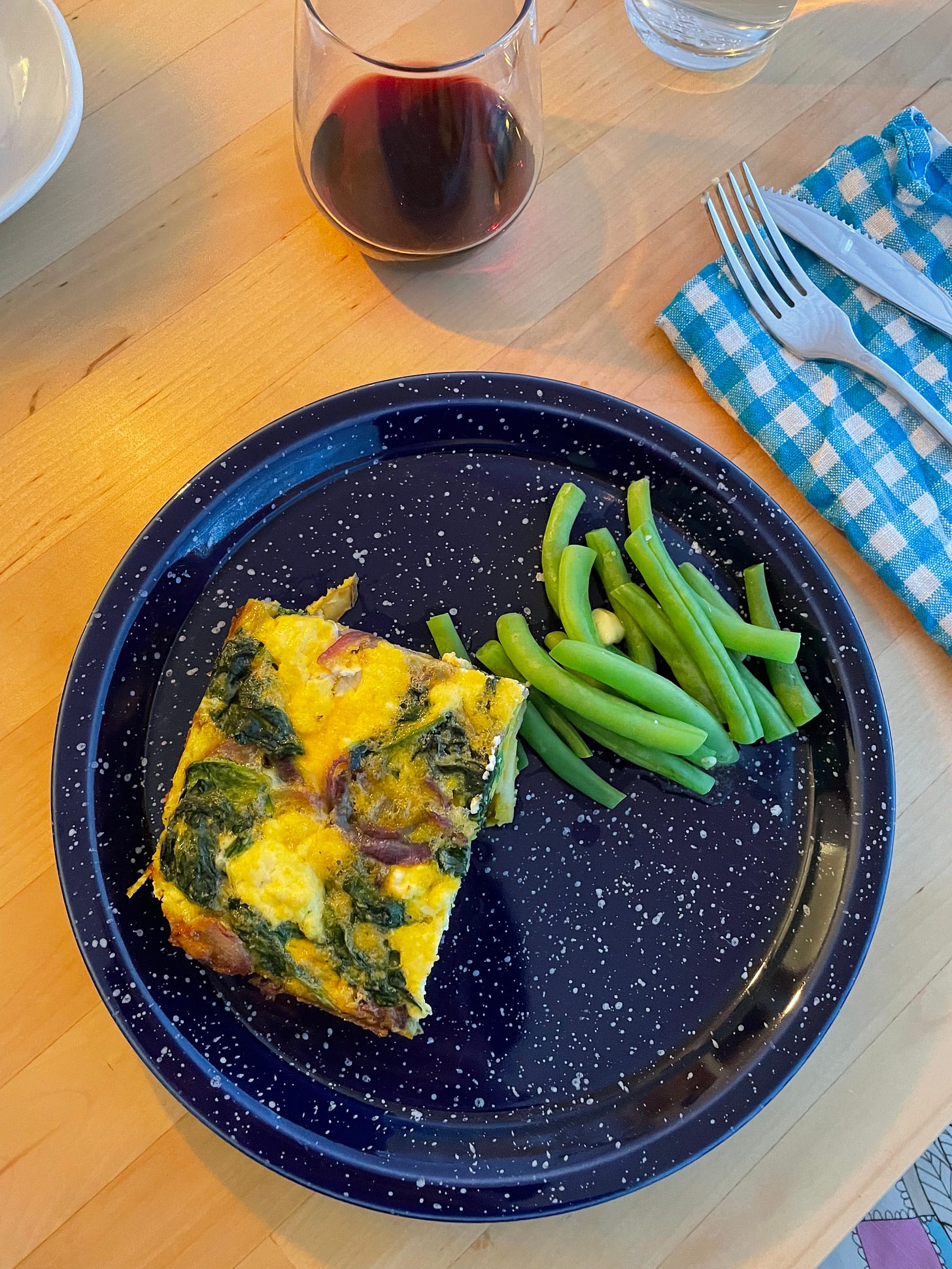Dinner plate with a slice of spinach, onion and goats cheese frittata with a side of green beans.