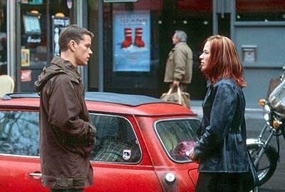 Still photo from the movie The Bourne Identity. Jason and Marie stand 4 feet apart staring intently at each other beside Marie's beat-up car on a Paris street.