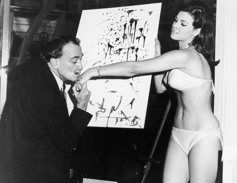 circa 1965: Spanish artist Salvador Dali (1904-1989) kisses American actor Raquel Welch's hand in front of his abstract portrait of her. Welch is wearing a bikini. (Photo by Hulton Archive/Getty Images)