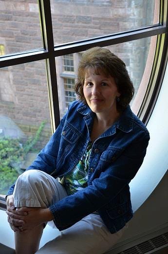 Photo of Julie Moore sitting on a windowsill in a denim jacket and smiling