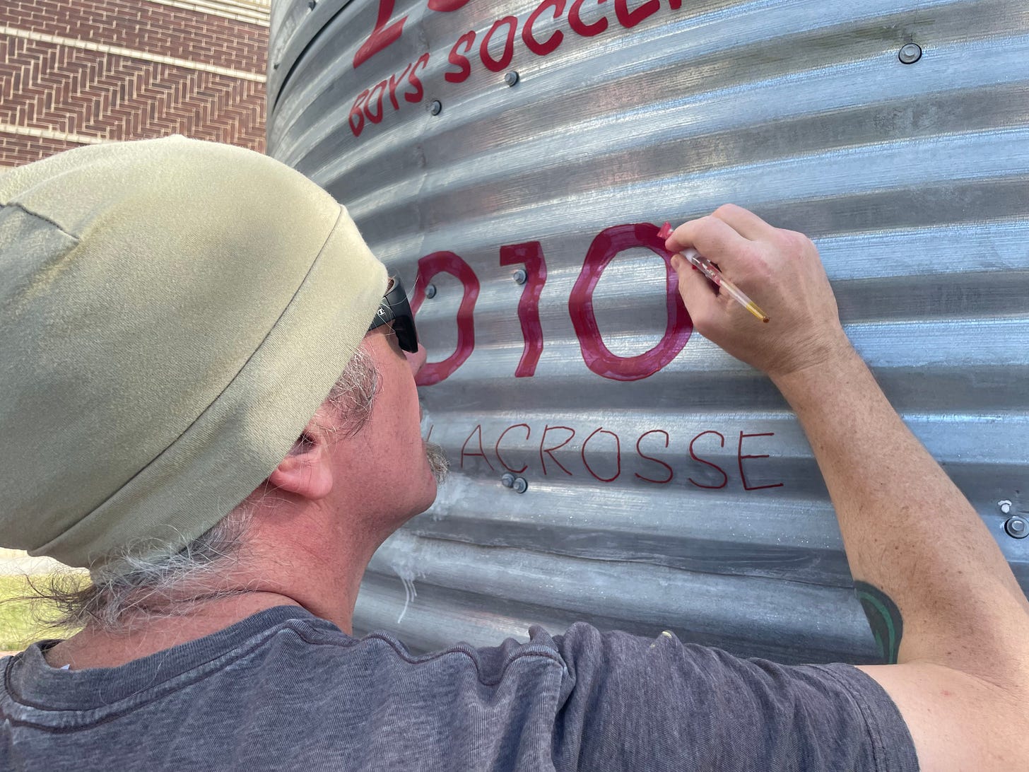 A man painting "2010 BOYS LACROSSE" on a silo