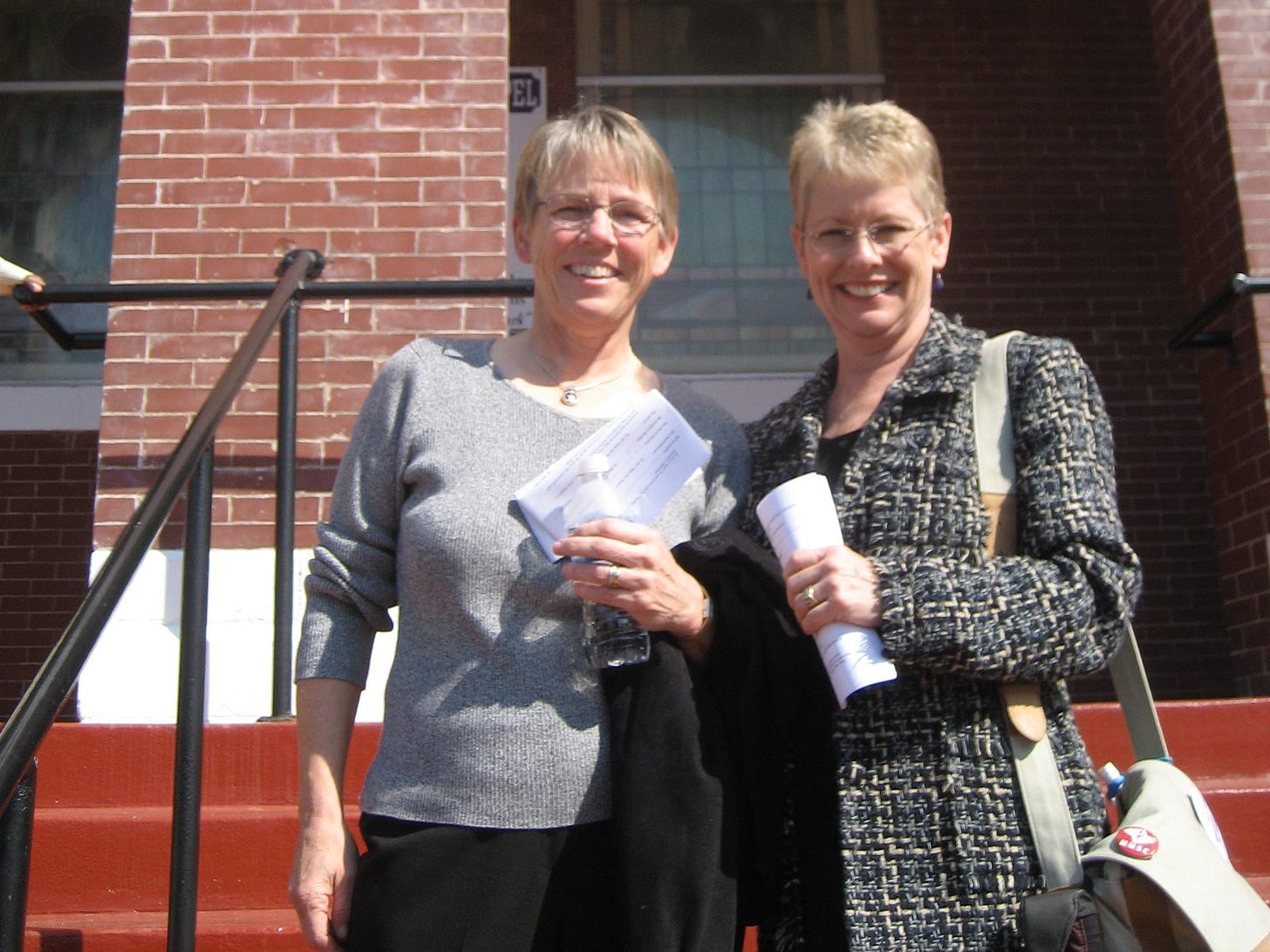 Two woman with short cropped blond hair standing on the steps of a church