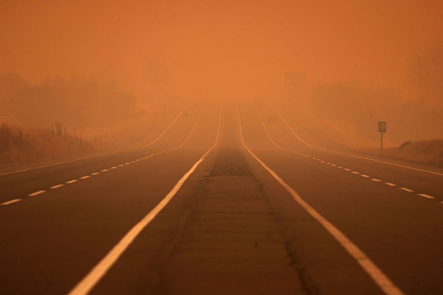 Smoke covers a road, coloring the sky orange.