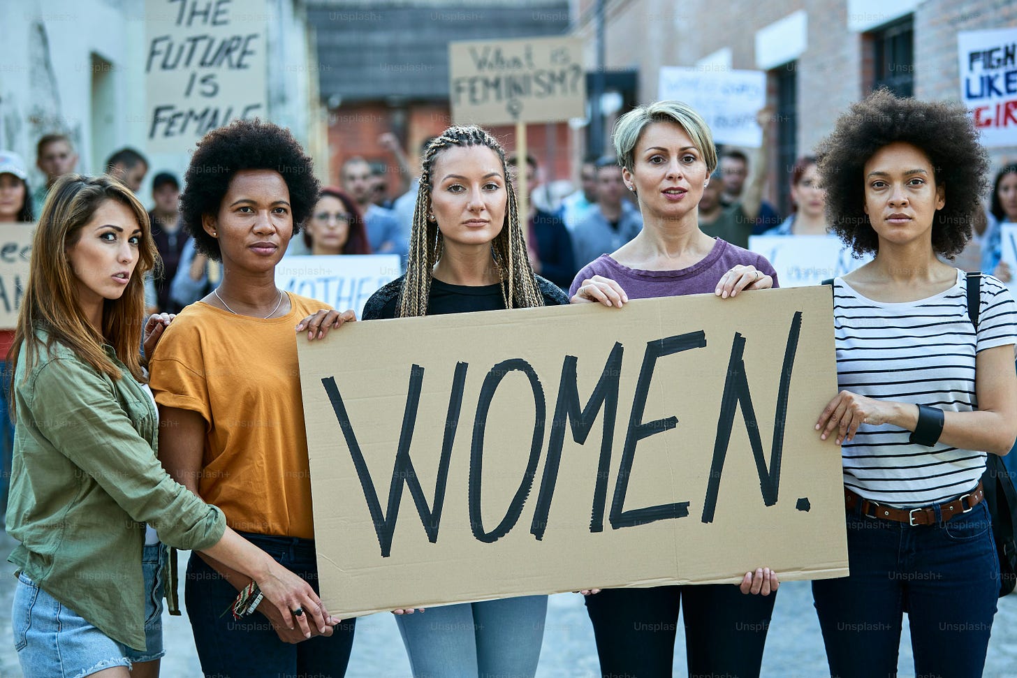 Group of females holding a banner with inscription 'women' while participating in street demonstrations.