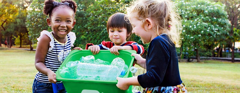 Three kids smiling and holding a box of empty plastic water bottles