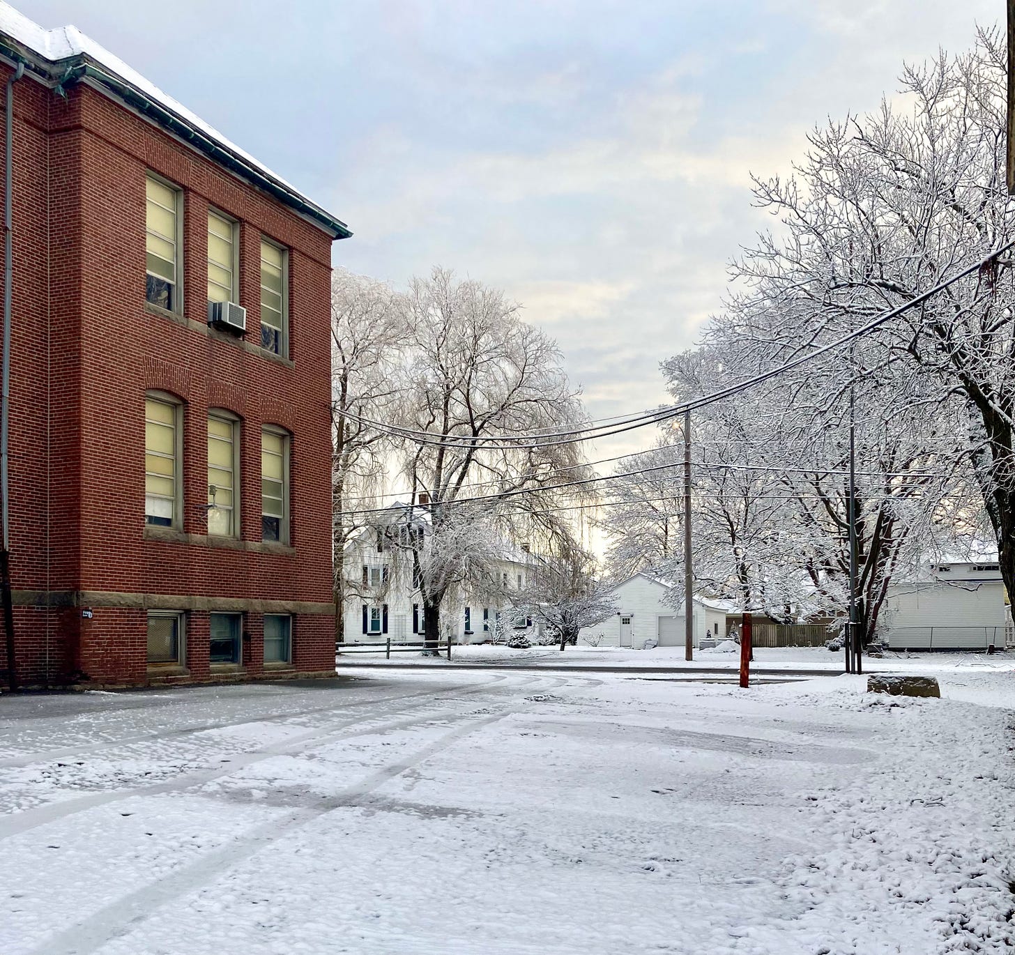 A morning scene of a snowy parking lot by a brick building