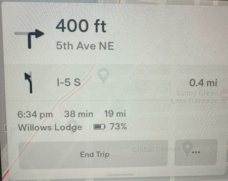 A photo of the Tesla navigation UI showing a set destination of Willows Lodge with an estimated time of 38 minutes and distance of 19 miles. The UI shows a predicted arrival battery level of 73%.