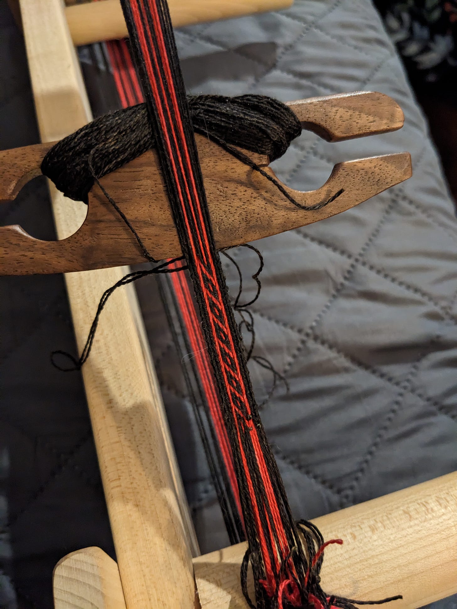 An inkle loom set up for card weaving with a pattern of black and red silk.