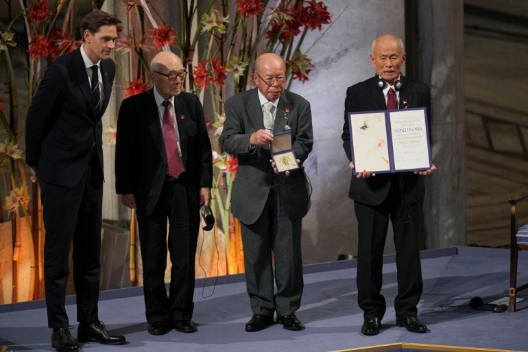 men in suits hold up a medal and a certificate in an ornatee hall