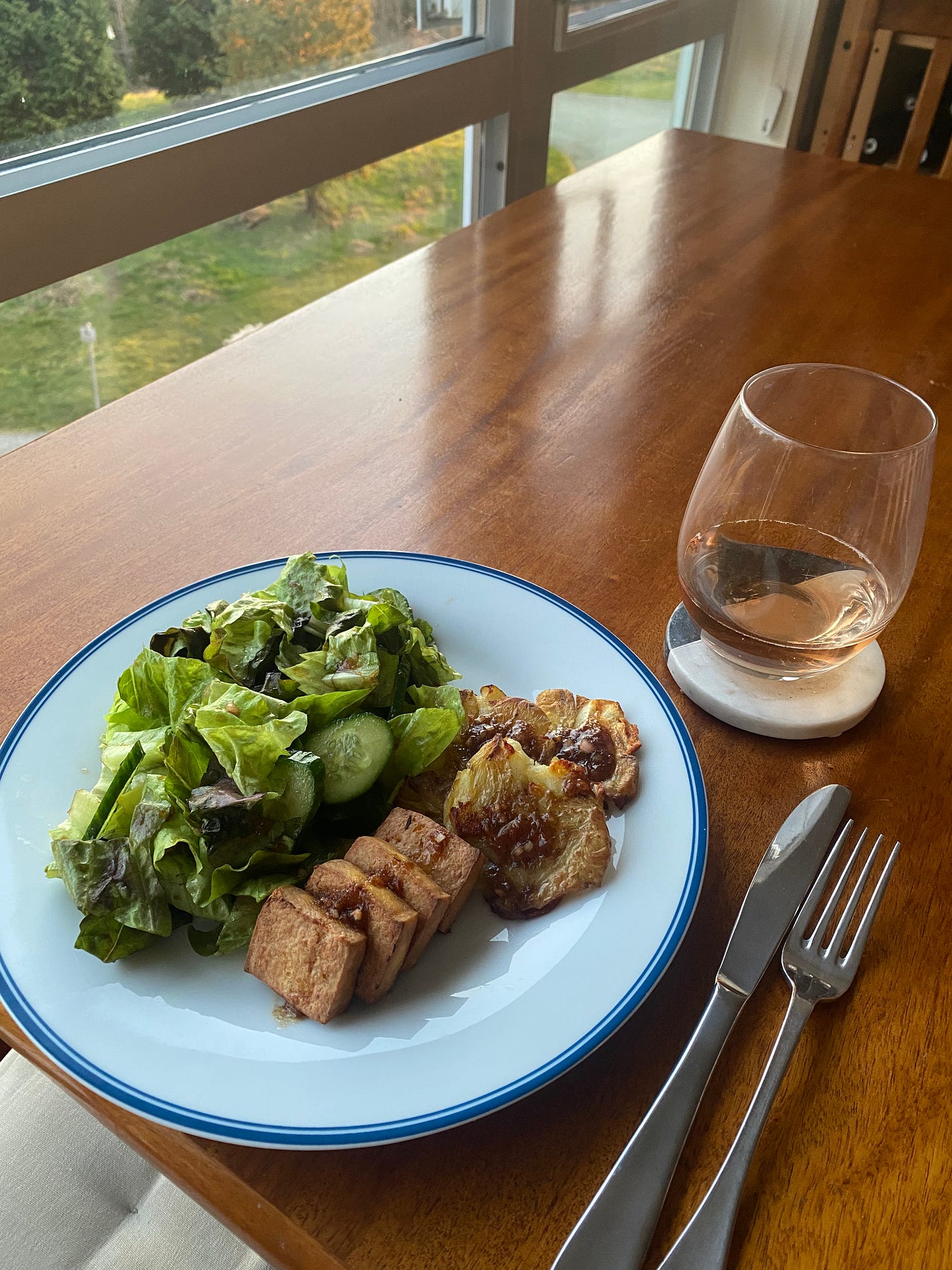 A plate of the salad, potatoes, and tofu described above, arranged with the salad on the left side and the other things in neat stacks or cascades on the other. The tomato dressing is drizzled over everything, and there is a stemless glass of rosé on a coaster next to the plate.