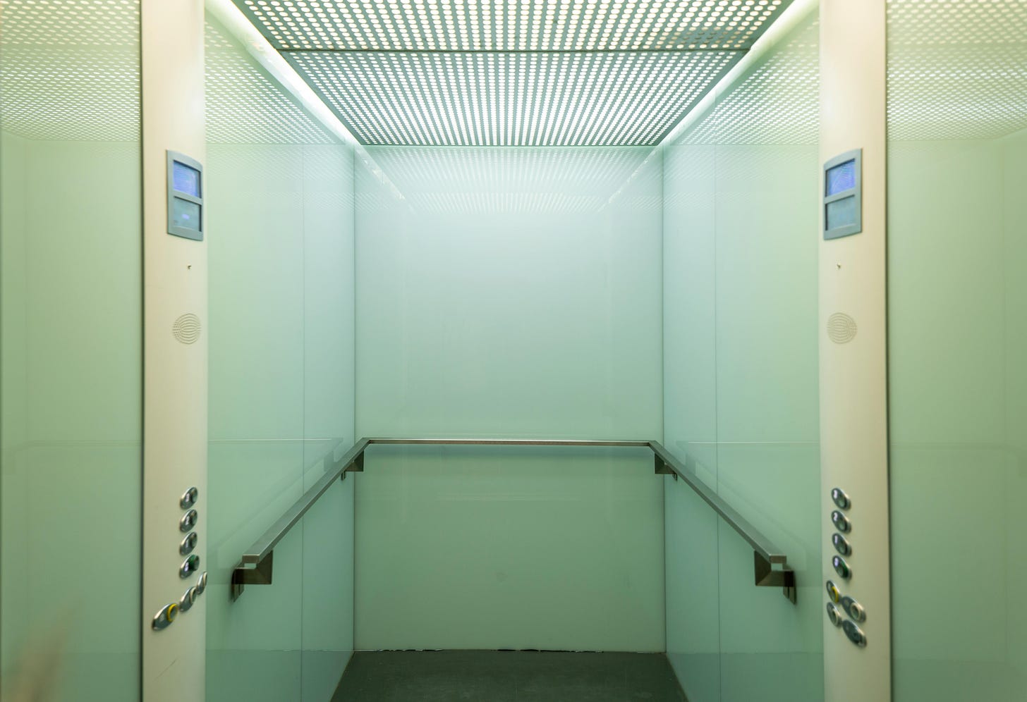 The inside of an empty elevator. The walls are lime green with yellow control panels.