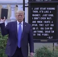 Convicted rapist Trump holding a bible upside down next to a sign that states the words he used in the Access Hollywood video: "I just start kissing them. It’s like a magnet. Just kiss. I don’t even wait. And when you’re a star, they let you do it. You can do anything. Grab ’em by the pussy. You can do anything."