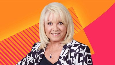 Elaine Paige shoulders and head are in shot and she is smiling.  She wears a black and white monochrome patterned blazer. The background of the image is the Radio 2 bright pink and orange graphics