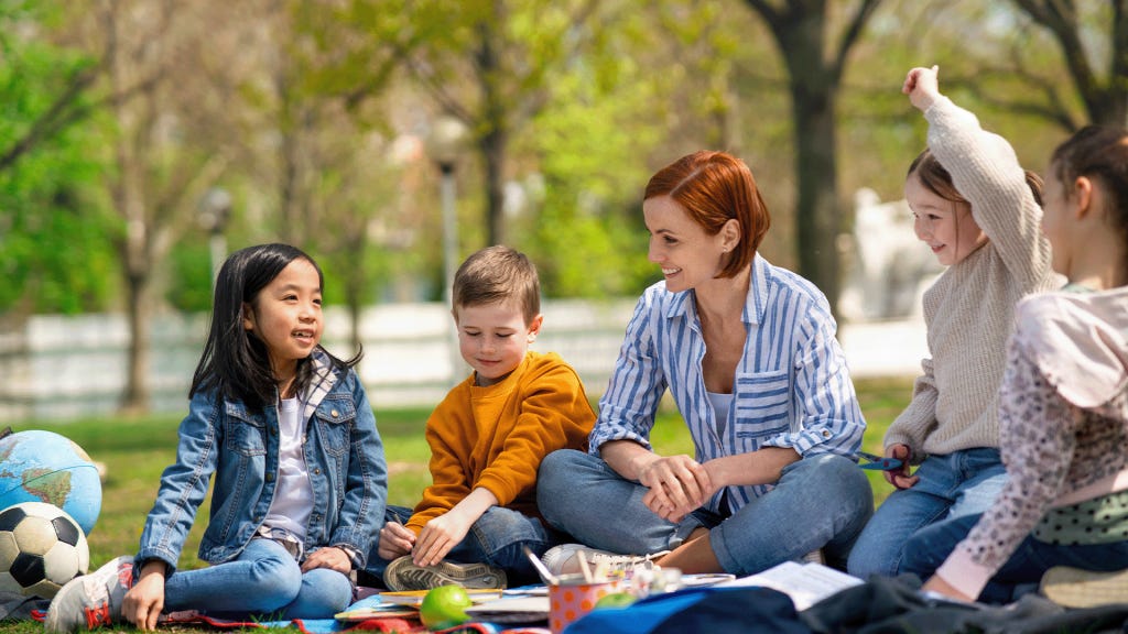 Teacher with children sitting outdoors in city park learning together