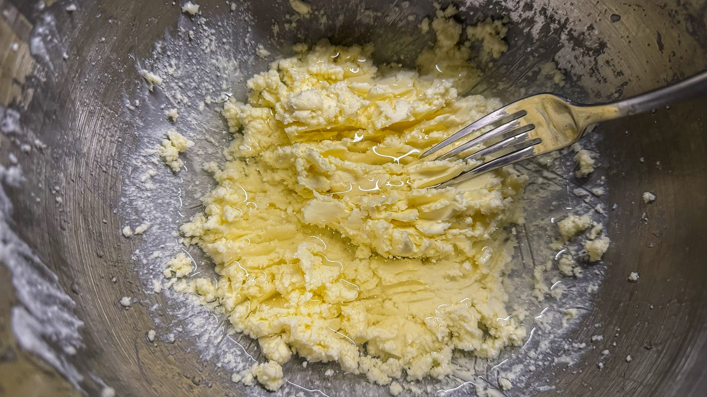 The end result of washing the butter. A fork has dragged streaks through the butter while clear unclouded water sits on top of it, indicating that all the buttermilk has been rinsed away. 