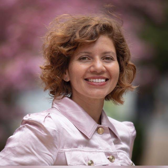 Image of a woman with short brown hair, brown skinned, wearing a light pink buttoned shirt.