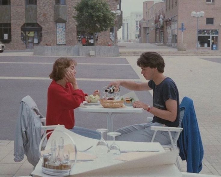 This may contain: two people sitting at an outdoor table eating food