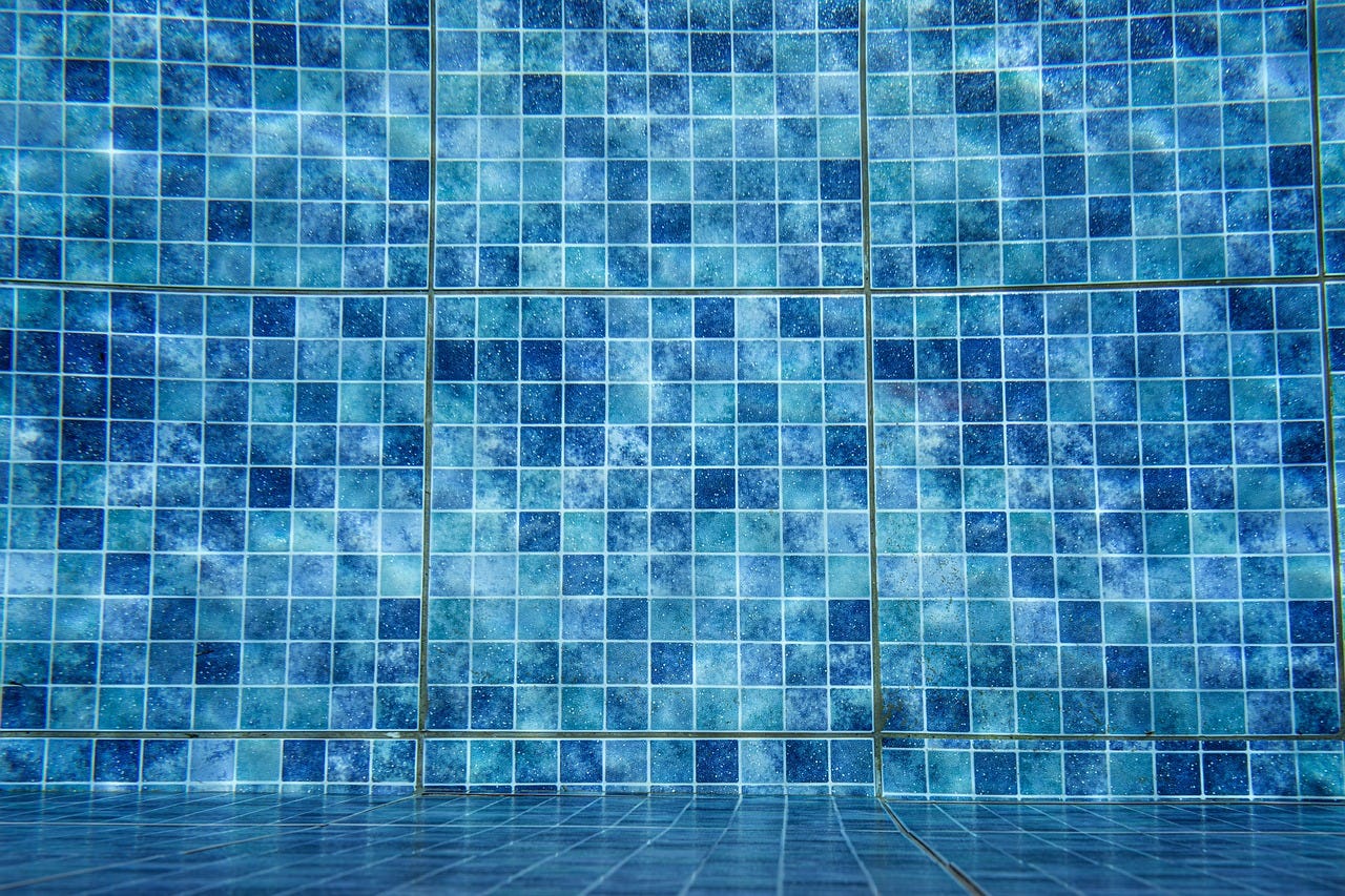 Fotografia de um fundo de piscina azulejado, azul, com ladrilhos que vão dos tons mais claros aos mais escuros