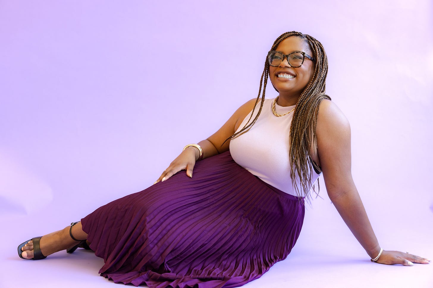 Picture of a Black woman wearing a dark purple skirt and a light purple top in front of a purple background Picture of a Black woman wearing a dark purple skirt and a light purple top in front of a purple background