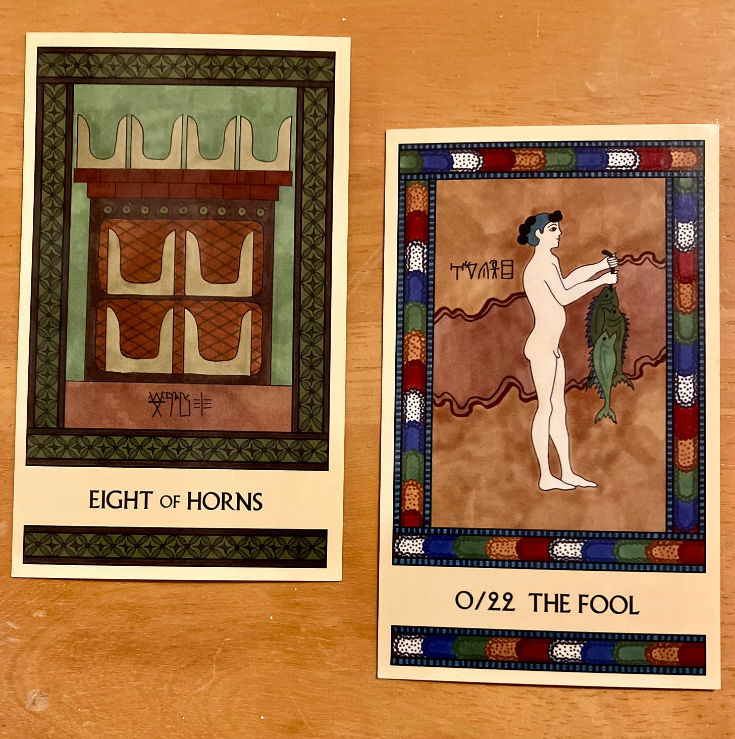 Two Minoan Tarot cards side by side on a golden wood surface. The Eight of Horns is painted in shades of green and brown. It shows eight pairs of Minoan sacred horns neatly arranged on a well-made, high quality shrine. The Fool has a bright multicolored border. It shows a Minoan young man, naked from just having been in the water. He is standing, facing right, holding up a larger string of fish.