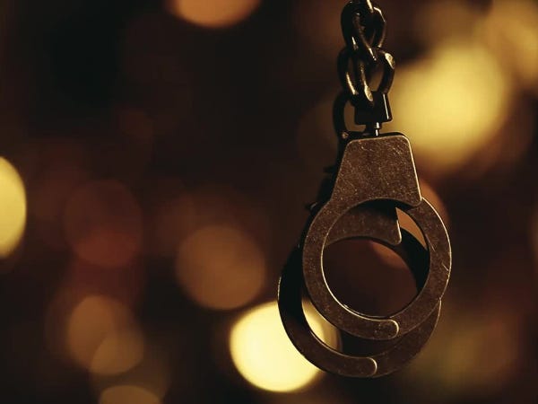 Handcuffs dangling against a blurred out background of gold lights