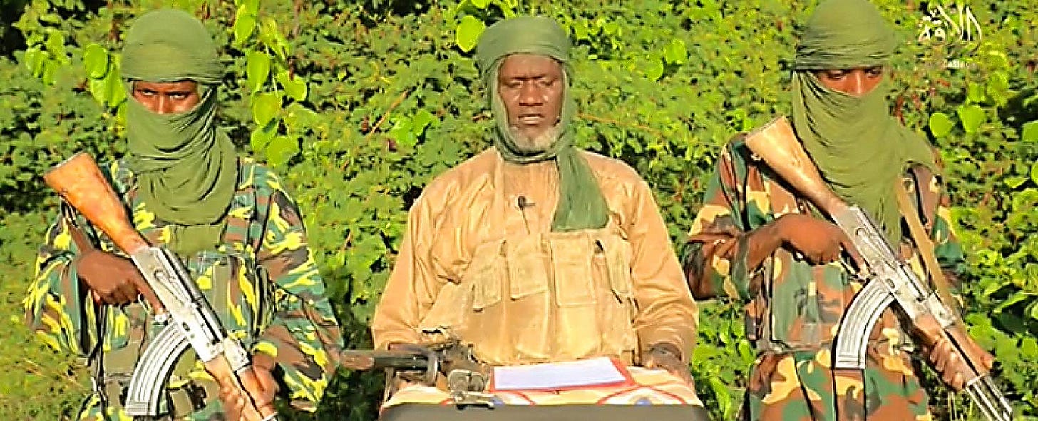 Koufa Mohamed Koufa stands and reads a message, flanked by two armed JNIM fighters.