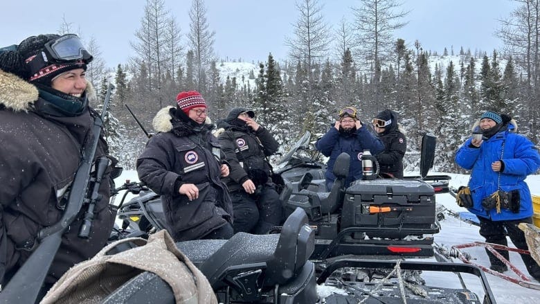 A group of six women snowmobilers smile and laugh on their machines outside in the winter in northern Quebec.