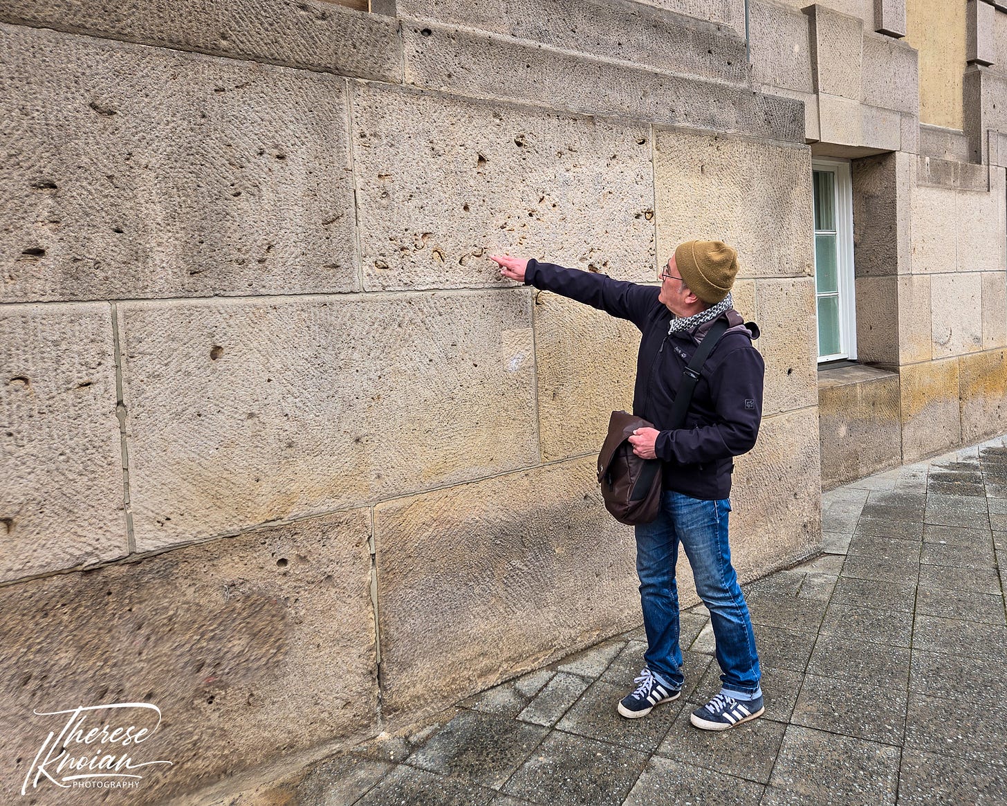 Peter Graham pointing out shrapnel marks in a building wall during a Berlin Battle Damage tour. 