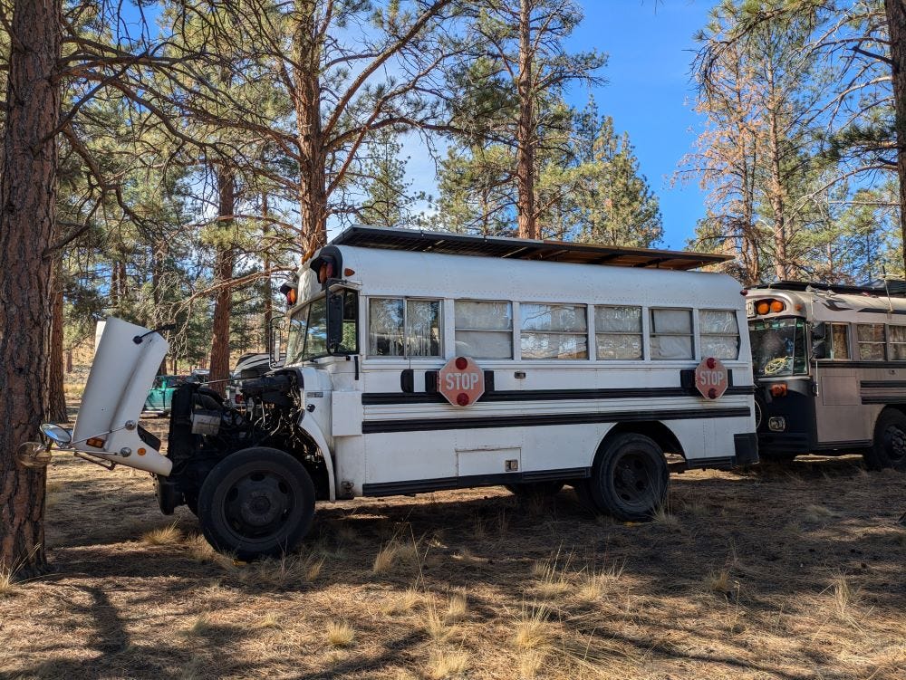 a short white school bus converted into a camper with the hood up for repairs or maintenance