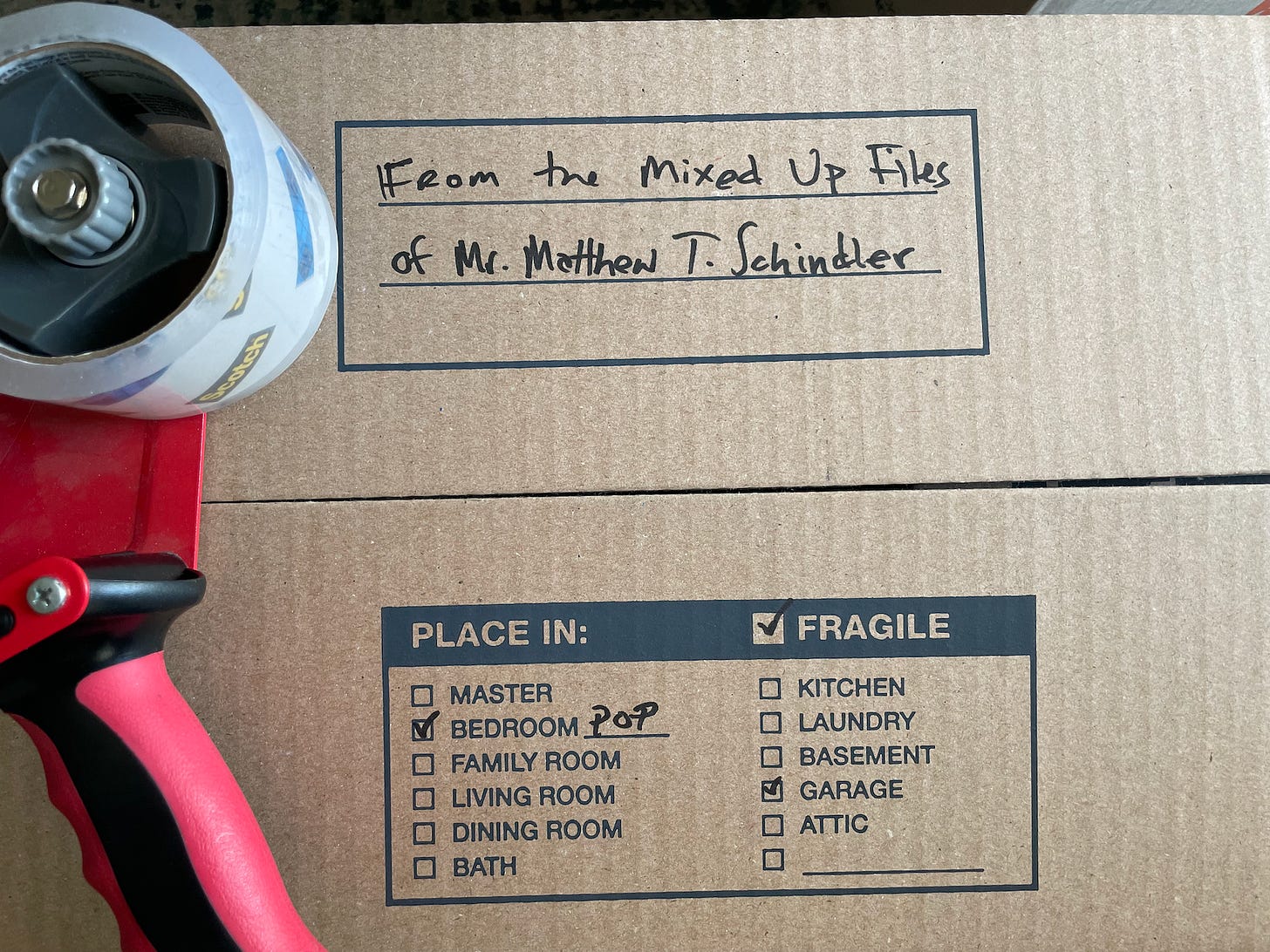 a cardboard moving box with "From the Mixed Up Files of Mr. Matthew T. Schindler writtten on it and Bedroom Pop, Garage, and Fragile