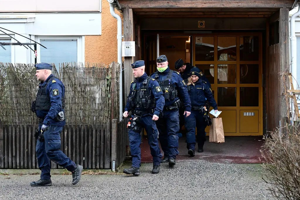 A line of uniformed police officers walking out of a residential-looking building with a yellow door.