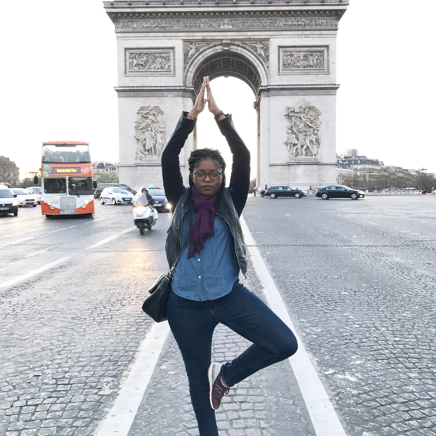 A Black woman standing in front of the Arc de Triomphe in Paris doing tree pose.