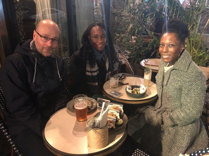 A man and two women sit at small tables with drinks outside the venue