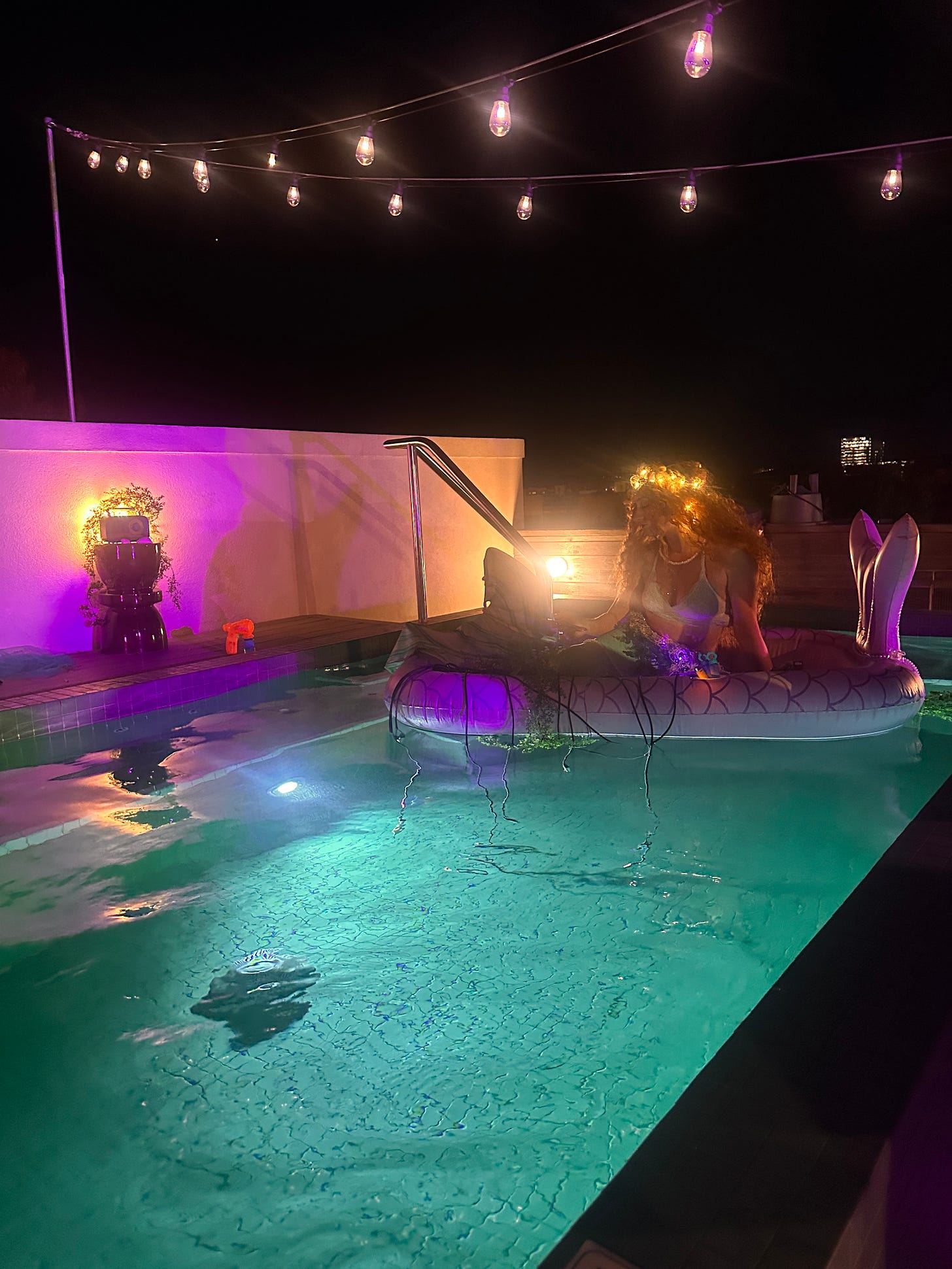 Image is of a rooftop pool which features Kaitlin Prest floating in a pool wearing a mermaid outfit