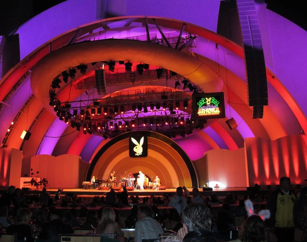 Hollywood Bowl lit up for the Playboy Jazz Festival with the playboy logo. Lights are red and pink. It is night and there is a band on stage