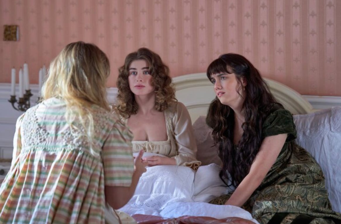Three women in Regency dress sit on a bed.