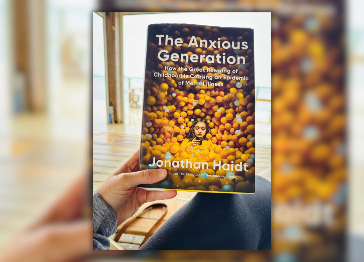 blurred background with a photo of a hand holding the book The Anxious Generation