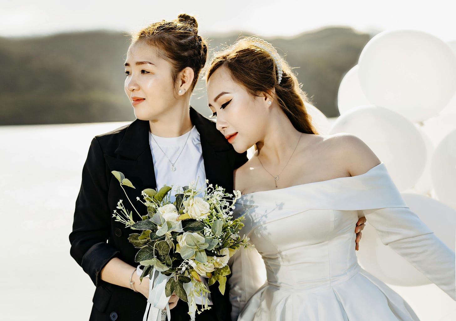 Two women, one in a blazer and another in a white wedding dress, pose for a bridal shot.