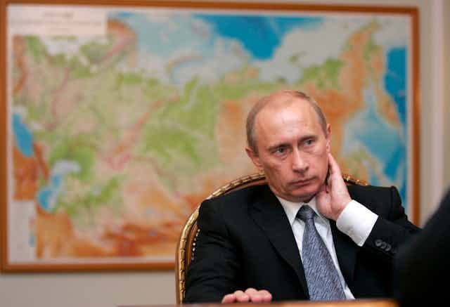 Vladimir Putin sitting in front of a map of Russia