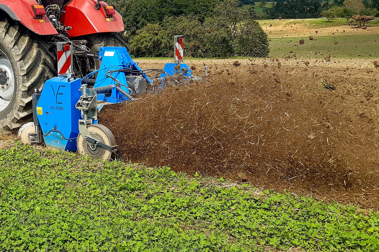 Eine Flachfräse des Typs VE A300 ist an einen Traktor gekoppelt und im Einsatz auf einem Acker. Die Maschine schneidet Pflanzenreste ab, zerkleinert sie und vermischt sie mit Erde. Im nächsten Schritt wird die entstandene Biomasse gleichmässig auf dem Feld verteilt – ein Verfahren der regenerativen Landwirtschaft zur Förderung der Bodenfruchtbarkeit. Eine Flachfräse des Typs VE A300 ist an einen Traktor gekoppelt und im Einsatz auf einem Acker. Die Maschine schneidet Pflanzenreste ab, zerkleinert sie und vermischt sie mit Erde. Im nächsten Schritt wird die entstandene Biomasse gleichmässig auf dem Feld verteilt – ein Verfahren der regenerativen Landwirtschaft zur Förderung der Bodenfruchtbarkeit.