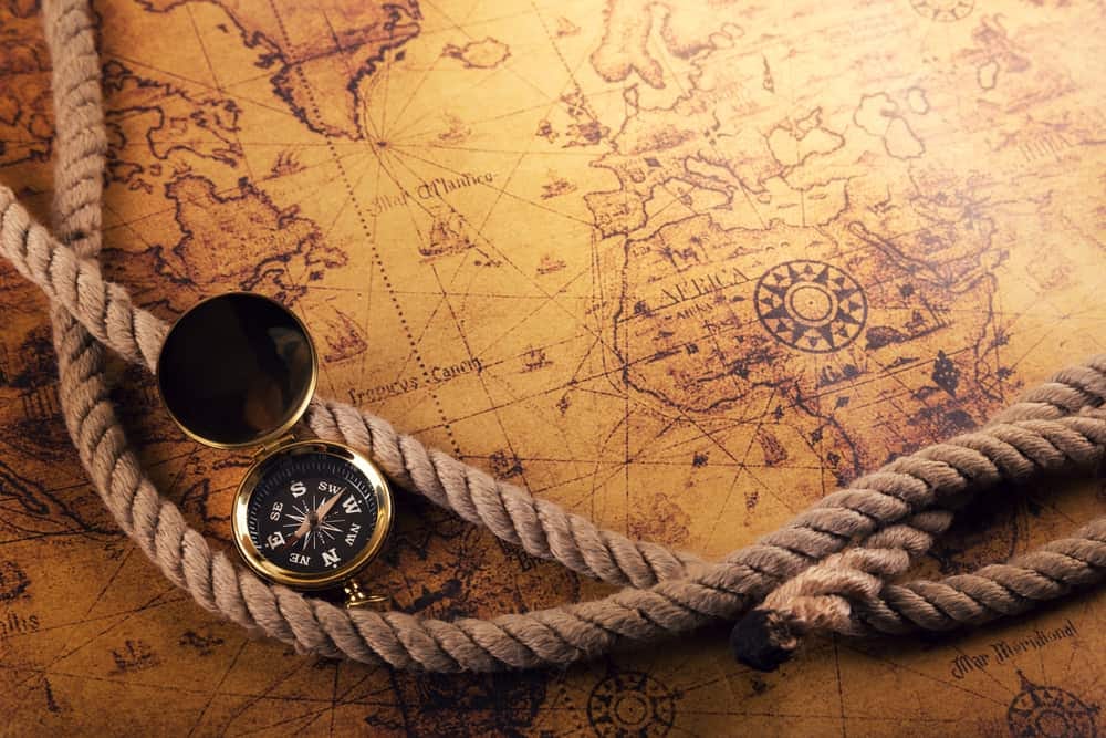 Sepia-toned map of the Atlantic Ocean with Africa and Europe most visible. Ship's rope and a compass are on top of the map.