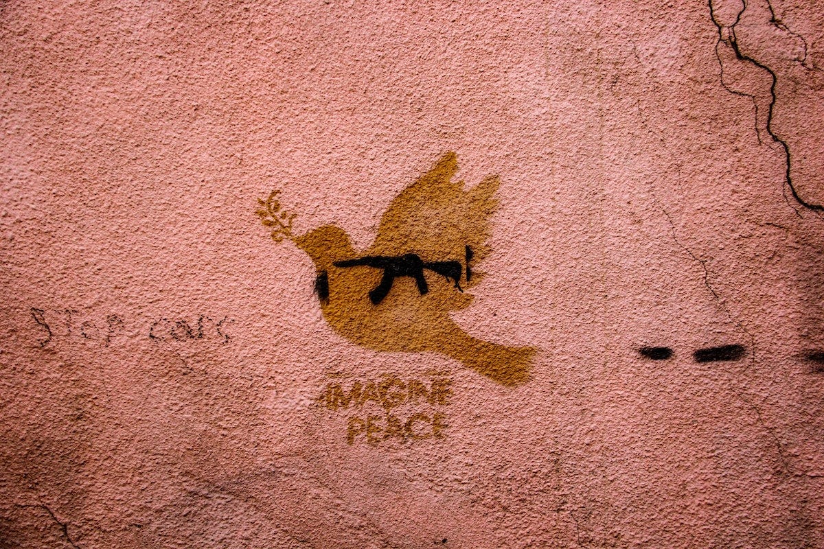 A dove painted on a wall with a gun painted over the dove. The words "imagine peace" are written below the dove and gun. 